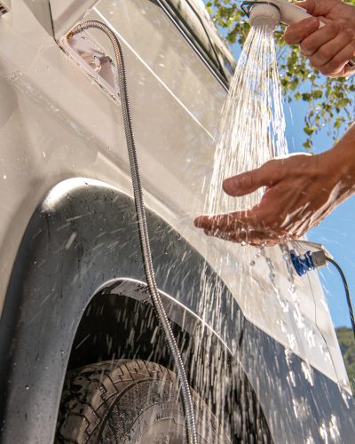 RV Camper Van Outdoor Shower Taking. Caucasian Men Preparing For Shower While on Wilderness Boondocking Camping. Recreational Vehicle Motorhome Outside Water Outlet.